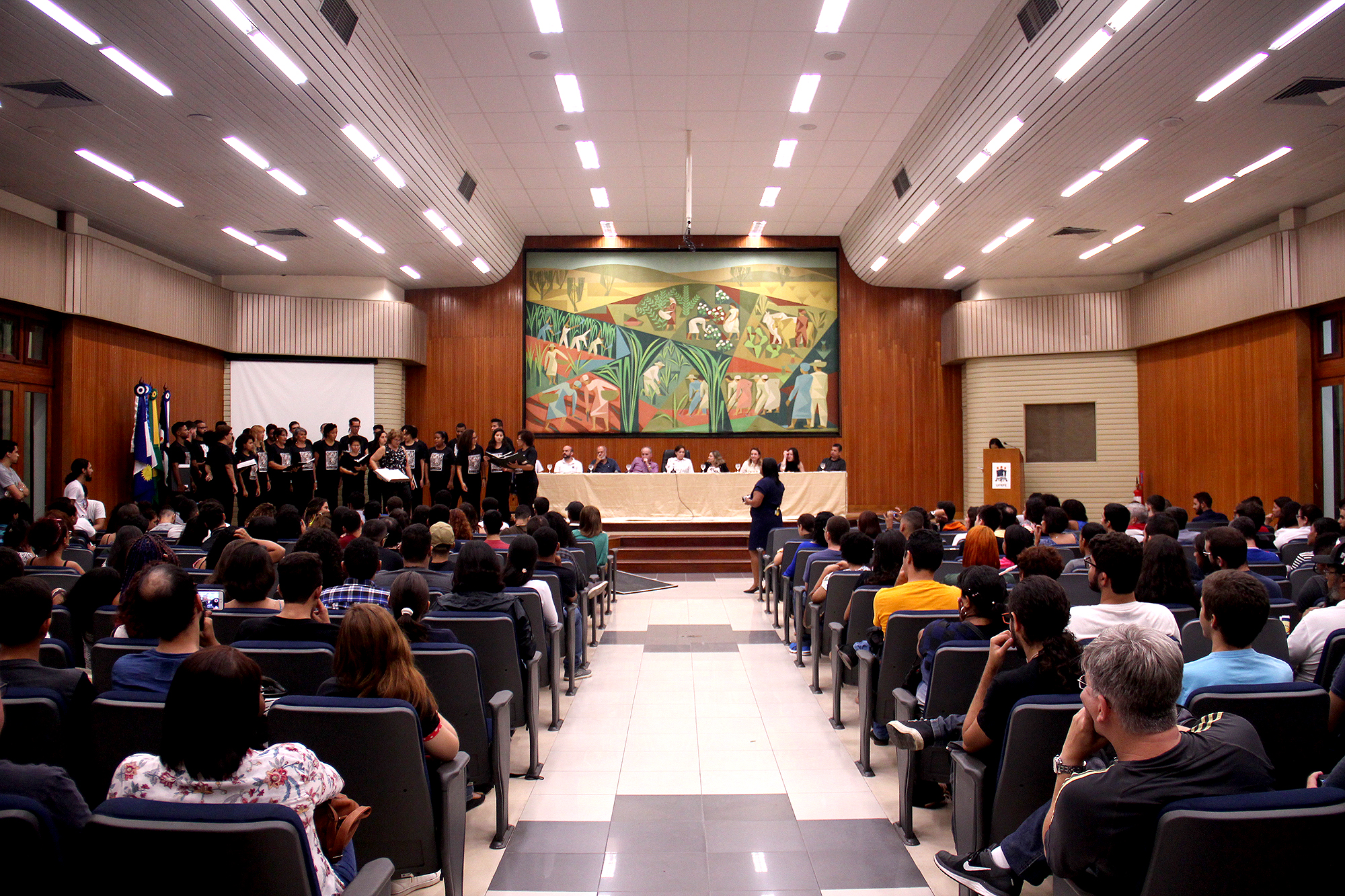Imagem da solenidade da Aula Inaugural, no Salão Nobre da UFRPE, estudantes sentados nas cadeiras no primeiro plano, mesa de autoridades ao fundo.